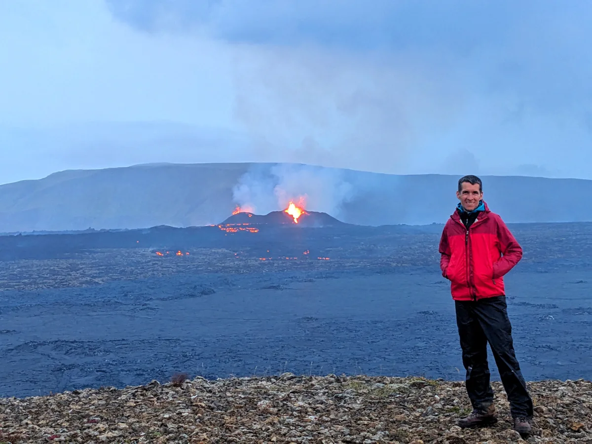 Simon on a volcanic trail with an active eruption in the distance